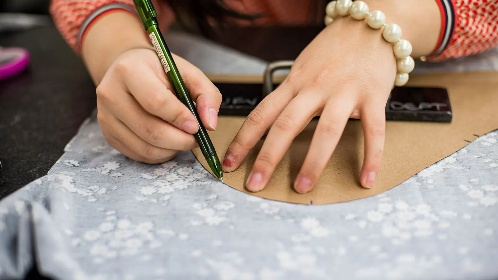 Hands tracing a paper pattern onto pale printed fabric with a pen on a cutting table