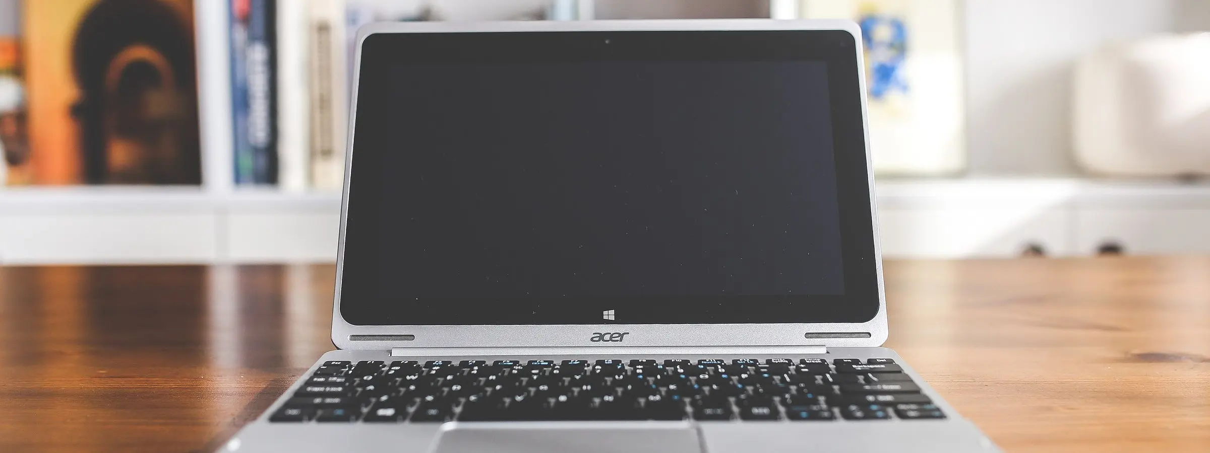 An open laptop on a polished wooden desk in front of shelves of books