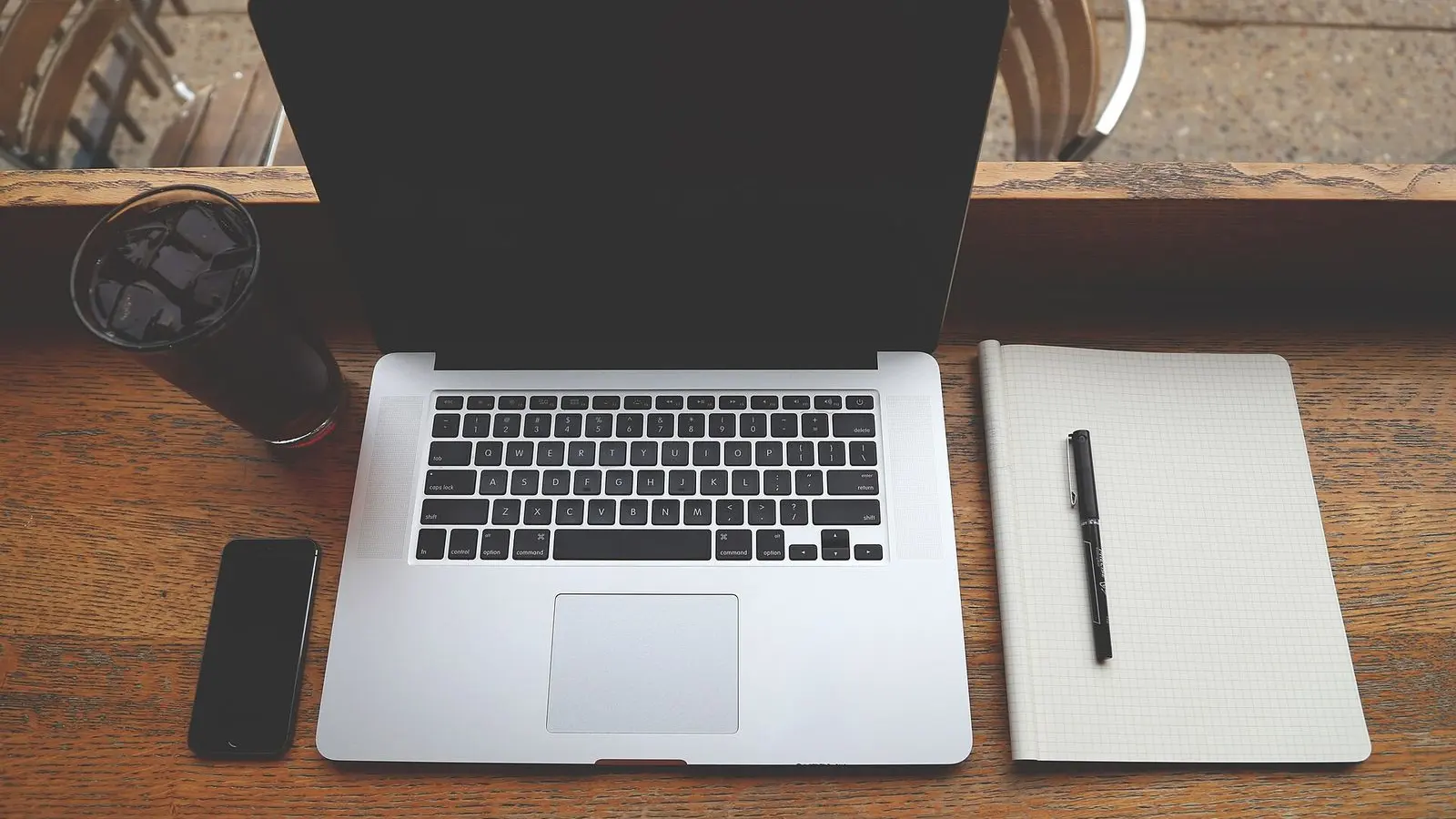A laptop, smartphone, notebook, pen and cup of coffee on a dark wooden desk