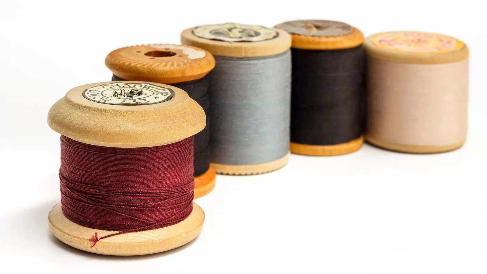 Wooden spools of sewing thread in red, cream, grey and black lined up in a row