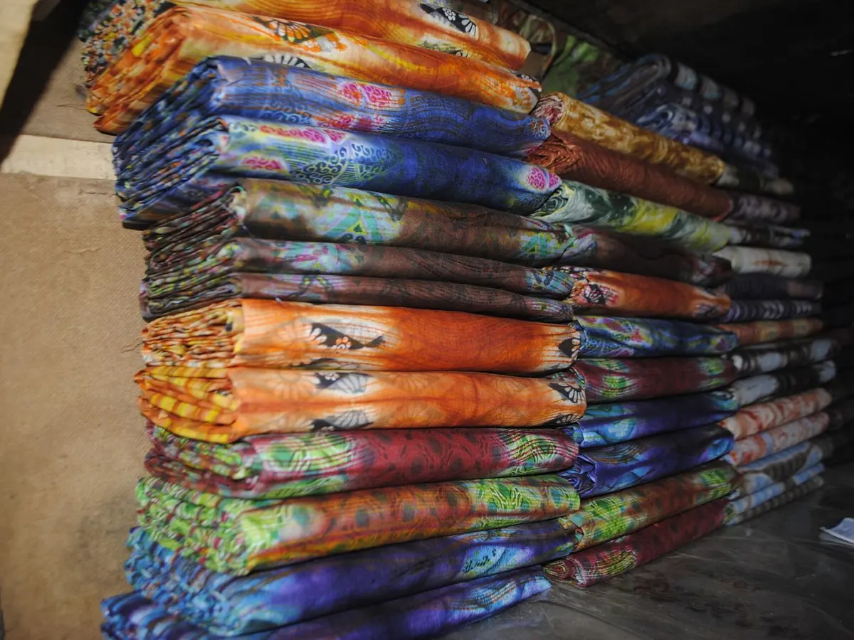 A tall stack of folded printed fabric in blue, orange and indigo patterns