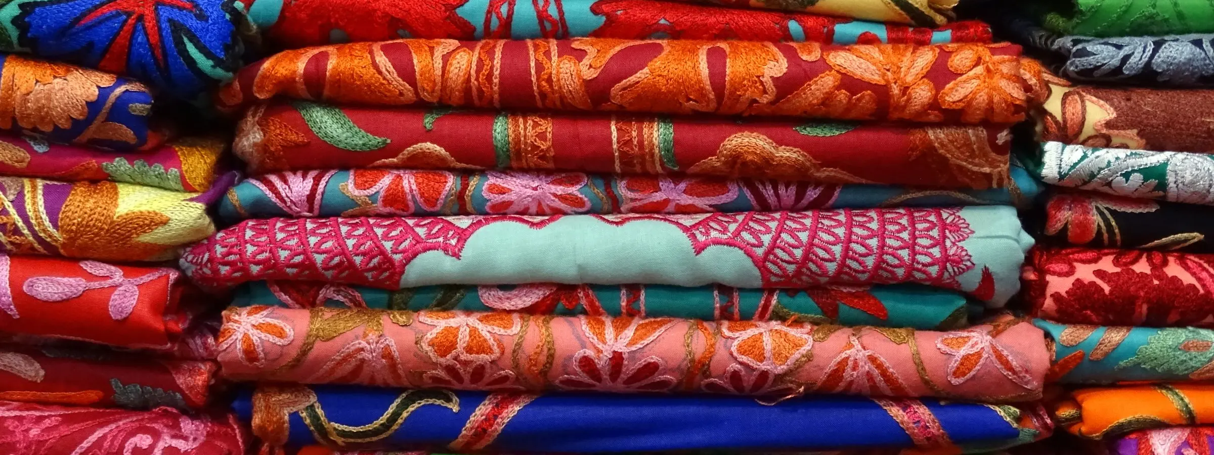 Folded lengths of bright patterned fabric piled on a shop counter in Manali