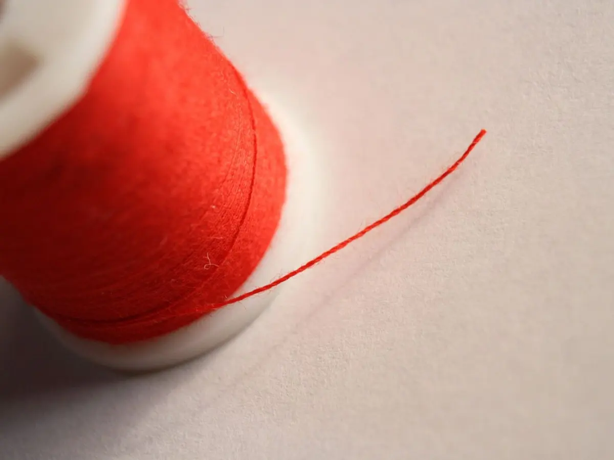 Close view of a spool of red thread with a loose end trailing across a white surface