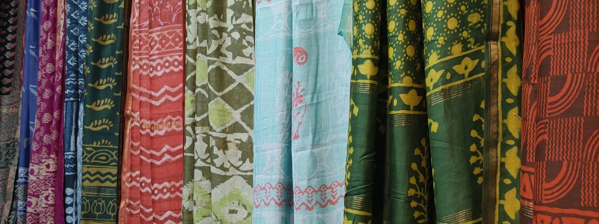 Lengths of block-printed kurta cloth in green, blue, red and rust hanging side by side in a shop