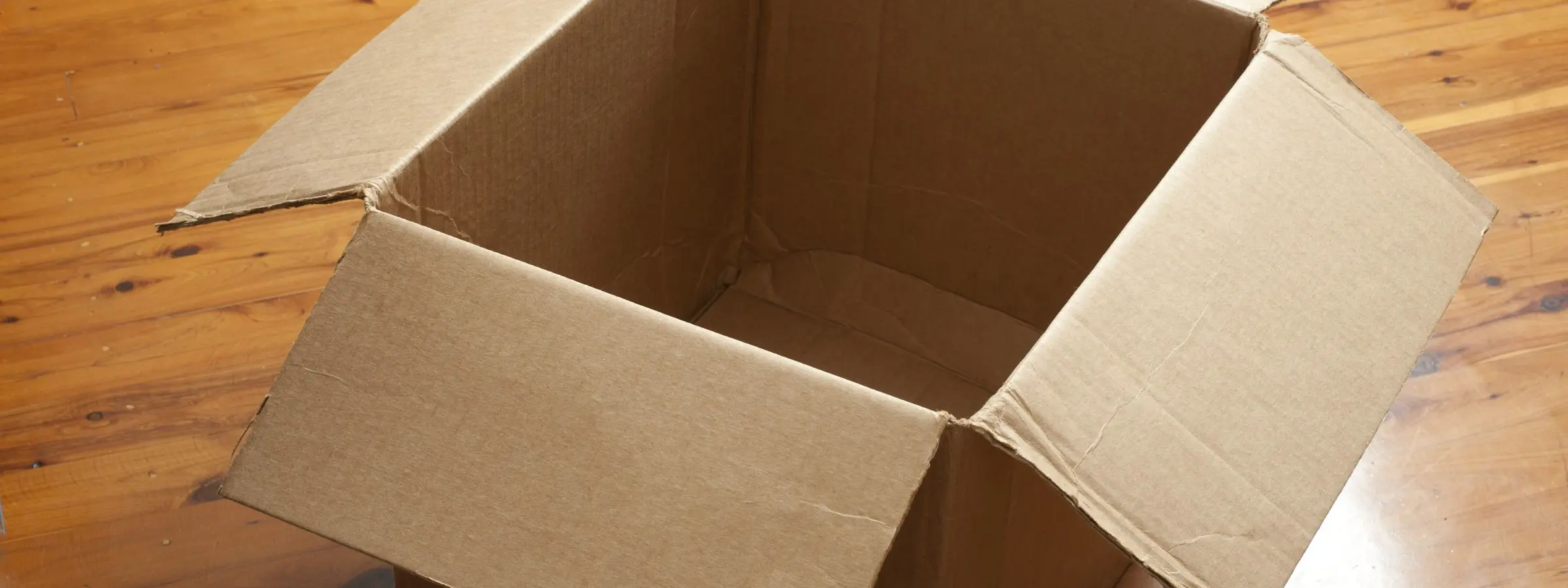 An empty cardboard box standing open on a polished wooden floor